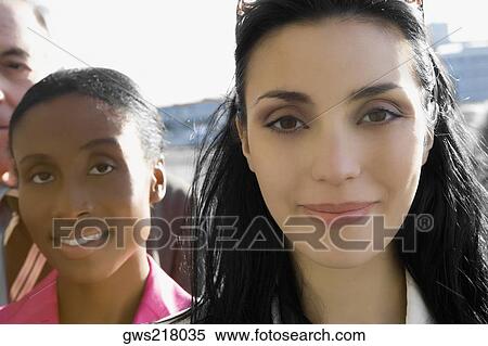 Stock Photography - Close-up of two businesswomen smiling with a businessman behind them. Fotosearch