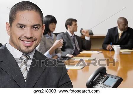 Portrait of a businessman smiling with his colleagues discussing in the background View Large Photo Image Stock Image - Portrait of a businessman smiling with his colleagues discussing in the background. Fotosearch