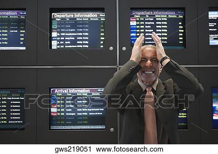 Stock Image - Businessman looking angry in front of an arrival departure board at an airport. Fotosearch