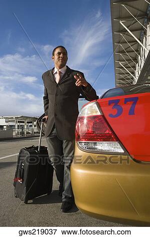 Businessman standing near a taxi with holding his luggage and gesturing View Large Photo Image Stock Photo - Businessman standing near a taxi with holding his luggage and gesturing. Fotosearch