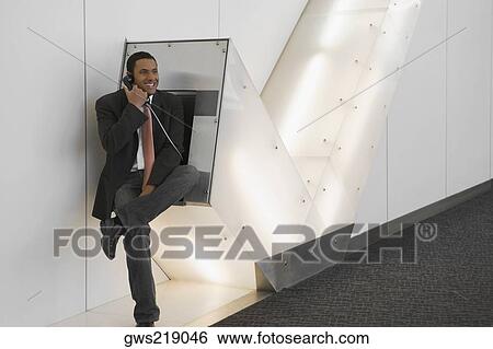 Businessman talking on a pay phone at an airport and smiling View Large Photo Image Stock Photograph - Businessman talking on a pay phone at an airport and smiling. Fotosearch