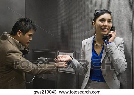 Stock Image - Businesswoman and a businessman talking on pay phones at an airport. Fotosearch