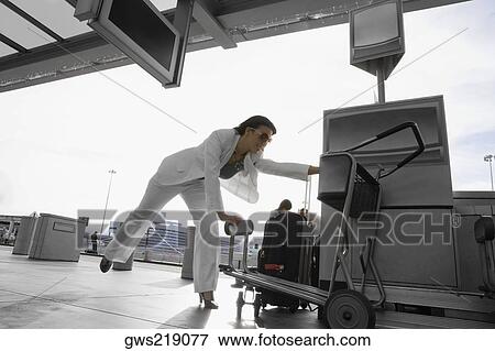 Businesswoman bending forward and holding her luggage cart at an airport View Large Photo Image Stock Photo - Businesswoman bending forward and holding her luggage cart at an airport. Fotosearch