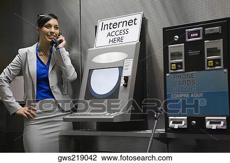 Stock Image - Businesswoman talking on a pay phone at an airport and smiling. Fotosearch