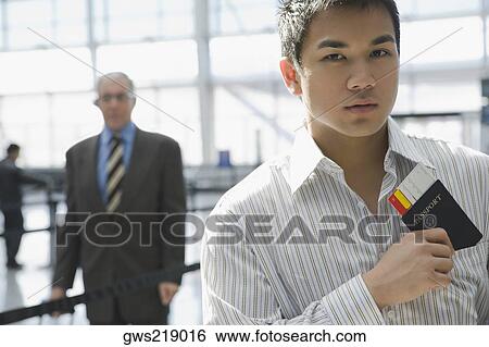 Stock Photograph - Close-up of a young man putting a passport with an airplane ticket in his shirt's pocket. Fotosearch