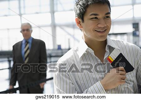 Stock Photography - Close-up of a young man putting a passport with an airplane ticket in his shirt's pocket. Fotosearch