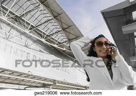 Low angle view of a businesswoman talking on a mobile phone outside an airport View Large Photo Image Stock Photograph - Low angle view of a businesswoman talking on a mobile phone outside an airport. Fotosearch