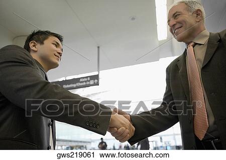 Stock Image - Low angle view of two businessmen shaking hands. Fotosearch