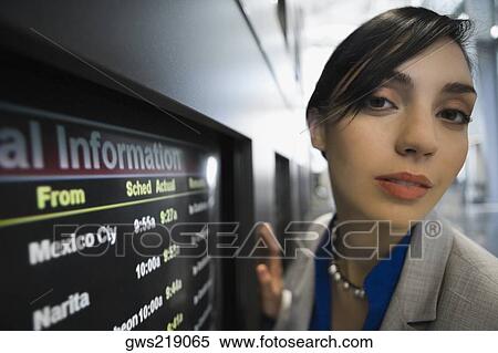 Stock Photography - Portrait of a businesswoman in front of an arrival departure board at an airport. Fotosearch