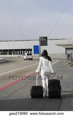 Stock Image - Rear view of a businesswoman pulling her luggage outside an airport. Fotosearch