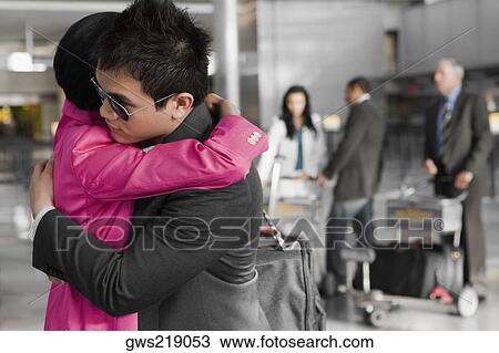 Stock Image - Side profile of a businessman and a businesswoman hugging each other at an airport. Fotosearch