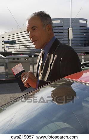 Stock Photo - Side profile of a businessman holding a passport with an airplane ticket. Fotosearch