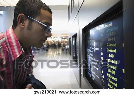 Side profile of a businessman looking at an arrival departure board in an airport View Large Photo Image Stock Image - Side profile of a businessman looking at an arrival departure board in an airport. Fotosearch