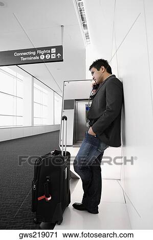 Stock Image - Side profile of a businessman talking on a pay phone at an airport. Fotosearch