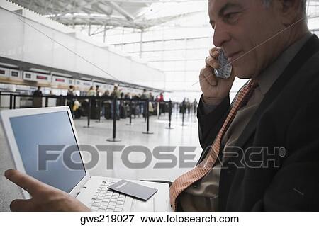 Side profile of a businessman talking on a mobile phone and using a laptop at an airport lounge View Large Photo Image Stock Photo - Side profile of a businessman talking on a mobile phone and using a laptop at an airport lounge. Fotosearch