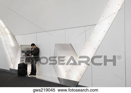 Stock Photography - Side profile of a businessman using a pay phone at an airport. Fotosearch