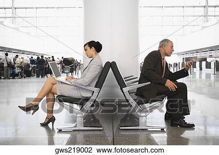 Side profile of a businesswoman using a laptop and a businessman using a mobile phone at an airport View Large Photo Image Stock Image - Side profile of a businesswoman using a laptop and a businessman using a mobile phone at an airport. Fotosearch
