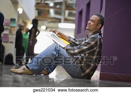 Side profile of a young man holding a textbook and sitting in a corridor View Large Photo Image Picture - Side profile of a young man holding a textbook and sitting in a corridor. Fotosearch