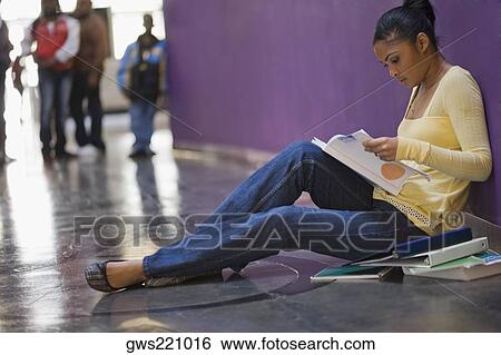 Stock Photograph - Side profile of a young woman reading a textbook in a corridor. Fotosearch