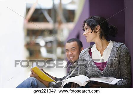 Stock Photo - Two university students leaning against a wall and holding textbooks. Fotosearch