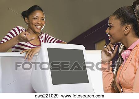 Stock Photo - Two young women looking at each other and smiling. Fotosearch