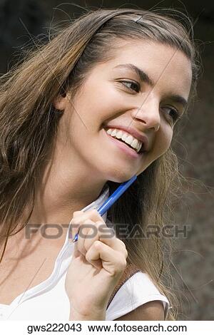 Close-up of a young woman holding a pen and smiling View Large Photo Image Stock Image - Close-up of a young woman holding a pen and smiling. Fotosearch