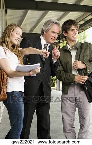 Male professor pointing with two university students standing beside him View Large Photo Image Stock Image - Male professor pointing with two university students standing beside him. Fotosearch