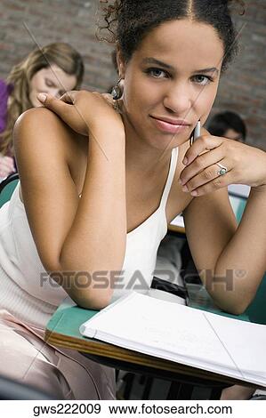 Portrait of a young woman studying in a classroom with her classmates in the background View Large Photo Image Stock Photo - Portrait of a young woman studying in a classroom with her classmates in the background. Fotosearch