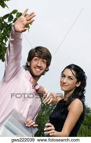 Young man waving hand with a young woman standing beside him View Large Photo Image Stock Photo - Young man waving hand with a young woman standing beside him. Fotosearch