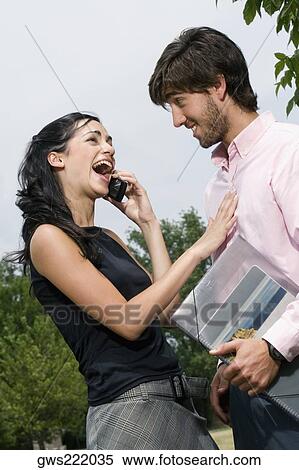 Young woman talking on a mobile phone with a young man standing beside her View Large Photo Image Stock Photography - Young woman talking on a mobile phone with a young man standing beside her. Fotosearch