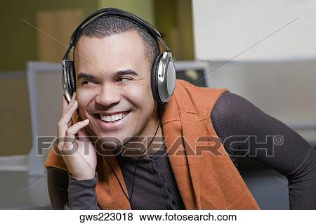 Close-up of a young man listening to music and smiling View Large Photo Image Stock Photo - Close-up of a young man listening to music and smiling. Fotosearch