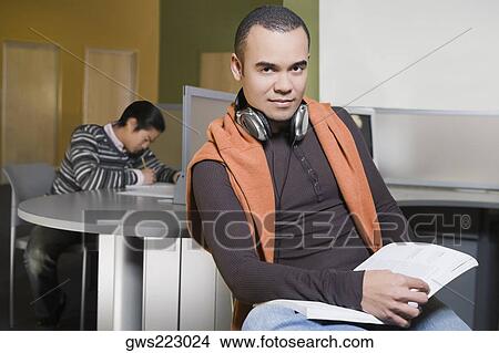Portrait of a young man holding a book in a computer lab View Large Photo Image Picture - Portrait of a young man holding a book in a computer lab. Fotosearch