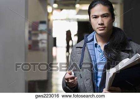 Portrait of a young man holding textbooks and a mobile phone View Large Photo Image Stock Photograph - Portrait of a young man holding textbooks and a mobile phone. Fotosearch