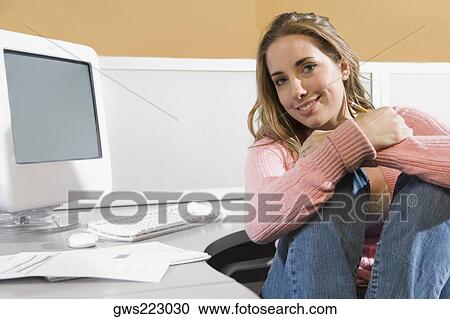 Portrait of a young woman sitting in front of a desktop PC and smiling View Large Photo Image Stock Image - Portrait of a young woman sitting in front of a desktop PC and smiling. Fotosearch