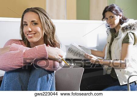 Portrait of a young woman smiling with another young woman sitting in the background View Large Photo Image Picture - Portrait of a young woman smiling with another young woman sitting in the background. Fotosearch