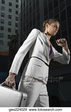 Stock Photo - Low angle view of a businesswoman walking and checking the time. Fotosearch