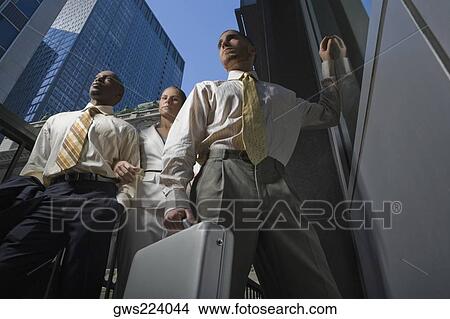 Low angle view of two businessmen and a businesswoman standing together View Large Photo Image Picture - Low angle view of two businessmen and a businesswoman standing together. Fotosearch
