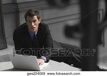 Portrait of a businessman sitting on steps and using a laptop View Large Photo Image Stock Photo - Portrait of a businessman sitting on steps and using a laptop. Fotosearch
