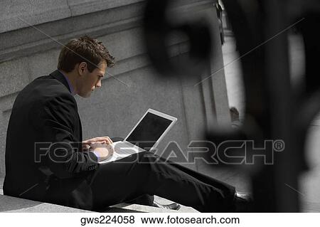 Side profile of a businessman sitting on steps and using a laptop View Large Photo Image Stock Photo - Side profile of a businessman sitting on steps and using a laptop. Fotosearch