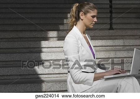Picture - Side profile of a businesswoman sitting on a staircase and using a laptop. Fotosearch