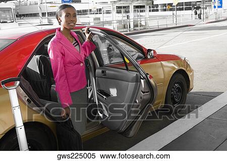 Stock Photography - Businesswoman standing near a taxi outside at an airport. Fotosearch