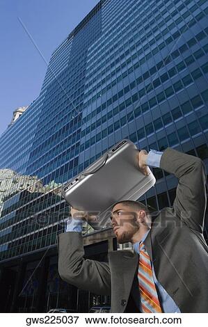 Stock Photo - Low angle view of a businessman using his briefcase as a shade. Fotosearch