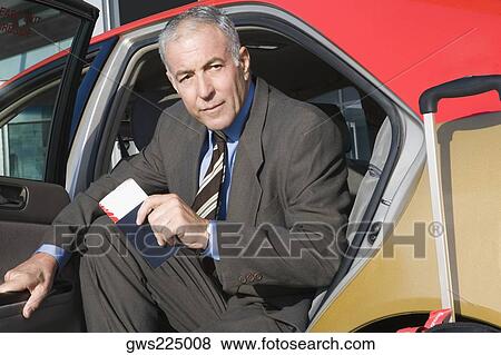 Stock Photo - Portrait of a businessman sitting in a taxi with holding a passport and an airplane ticket. Fotosearch