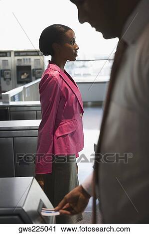 Stock Image - Side profile of a businessman checking his ticket into a check-in machine with a businesswoman standing beside him. Fotosearch