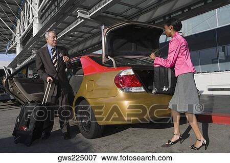 Side profile of a businesswoman loading her suitcase on a car trunk with a businessman standing in front of her View Large Photo Image Stock Photo - Side profile of a businesswoman loading her suitcase on a car trunk with a businessman standing in front of her. Fotosearch