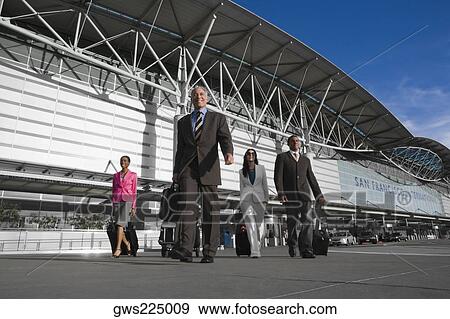 Stock Photo - Two businessmen with two businesswomen walking outside at an airport. Fotosearch