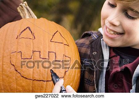 Boy drawing a human face on a pumpkin View Large Photo Image Stock Image - Boy drawing a human face on a pumpkin. Fotosearch