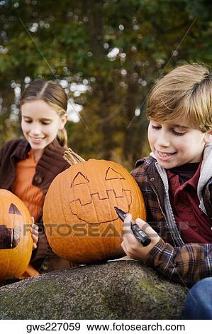 Boy drawing a human face on a pumpkin with his sister sitting behind him View Large Photo Image Stock Photo - Boy drawing a human face on a pumpkin with his sister sitting behind him. Fotosearch