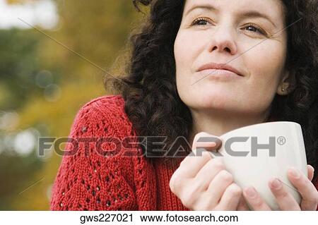 Stock Image - Close-up of a mid adult woman holding a coffee cup and thinking. Fotosearch