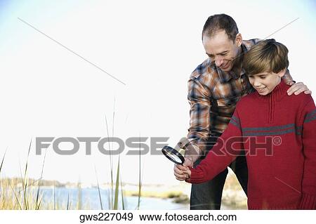 Low angle view of a mid adult man with his son holding a magnifying glass View Large Photo Image Stock Photo - Low angle view of a mid adult man with his son holding a magnifying glass. Fotosearch